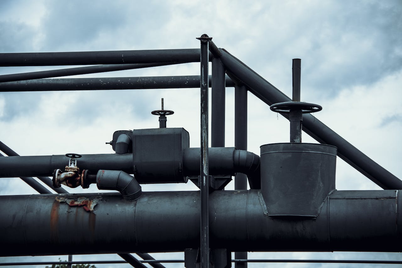 services-03 Close-up of industrial pipes and valves with rusty sections against a cloudy sky background.