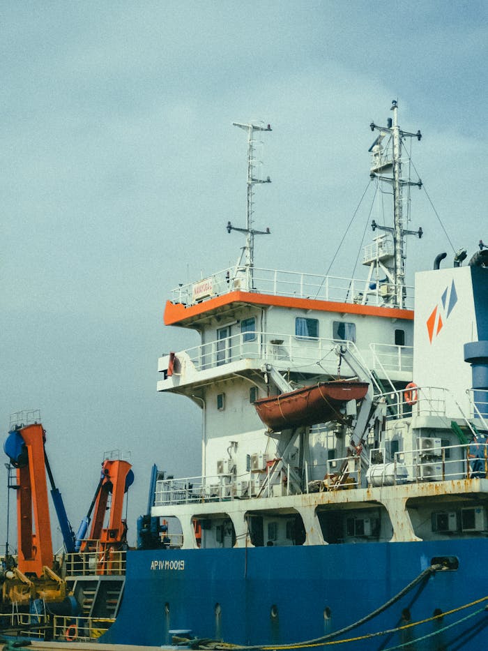 Large cargo ship docked at port with visible cranes and clear sky.