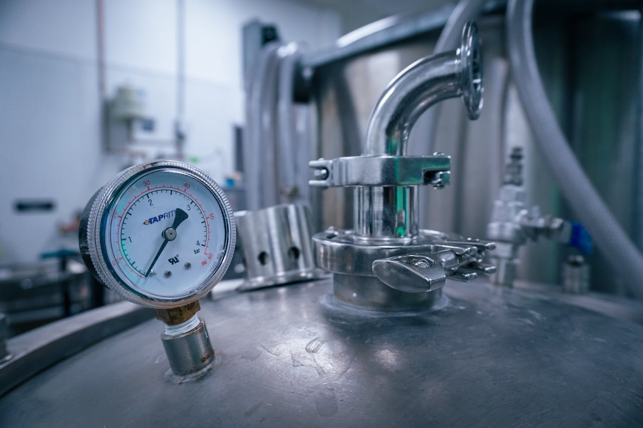 team-02 Close-up of a pressure gauge on a stainless steel tank in a sterile industrial setting, showcasing manufacturing technology.